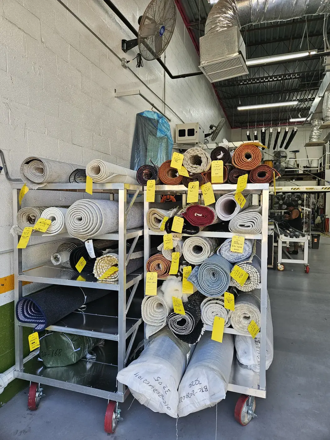 Rolled rugs on plant racks tagged with individual work orders